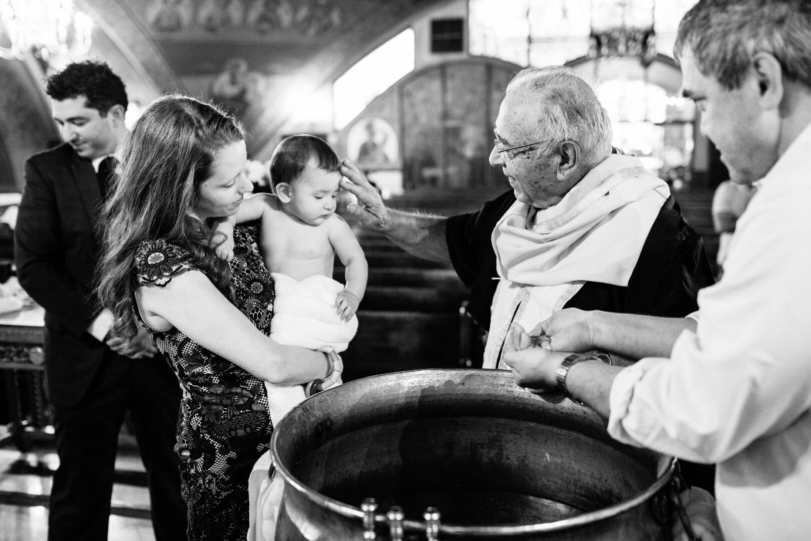 A baptism ceremony unfolds in a New York City church, with a priest performing the rite on a baby held by a woman, as two men stand nearby. Perfect for capturing cherished New York City baptism photos.