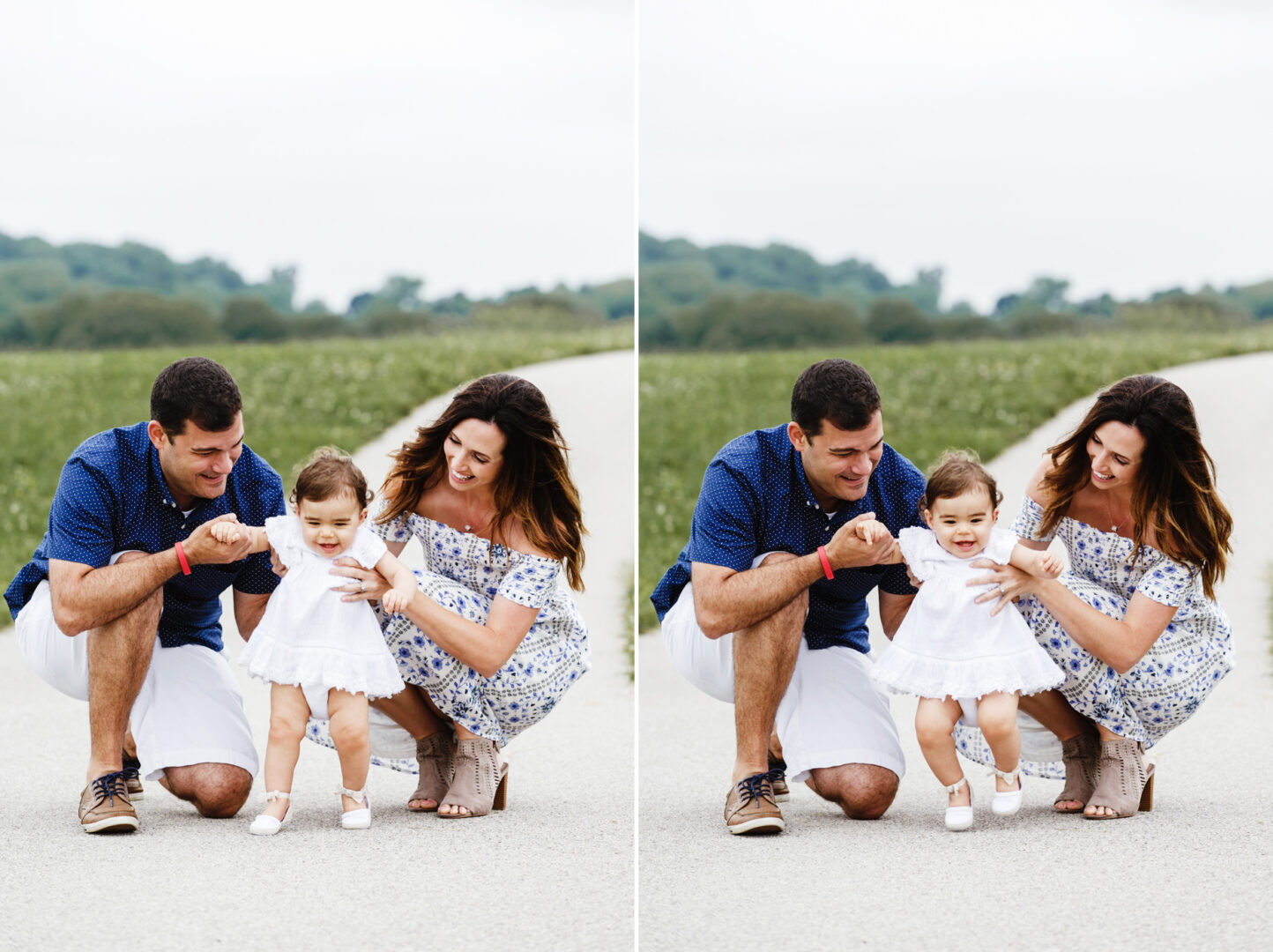 A couple kneels on a rural road, holding the hands of a delighted toddler celebrating their first birthday, standing between them and smiling. The backdrop features lush green fields and a cloudy sky, perfectly setting the scene for a memorable cake smash moment.
