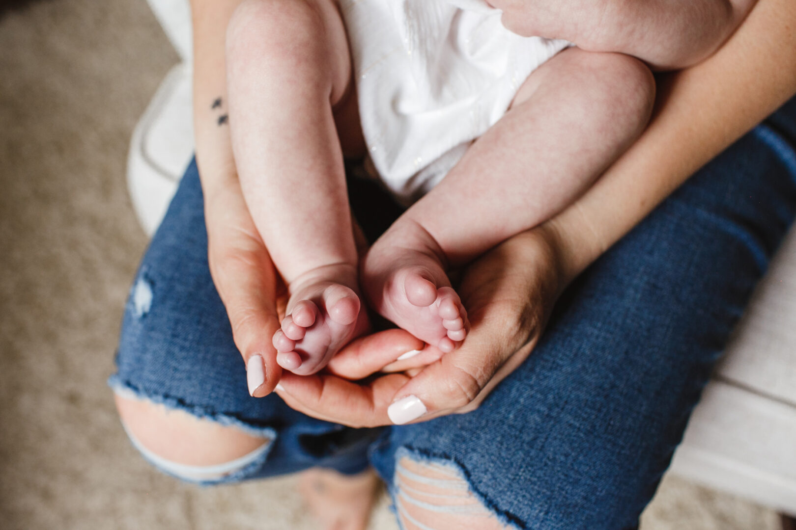 Close-up of a baby’s legs and feet resting gently on an adult's hands, framed against the backdrop of ripped jeans. Captured for a precious moment in Philadelphia, this image embodies the tender beauty found in newborn photos.