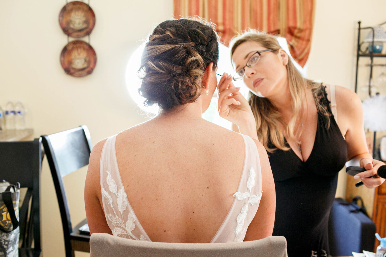 At Seaport Pier, a makeup artist skillfully applies eye makeup to a woman in a sleeveless dress, complementing her intricate hairstyle.
