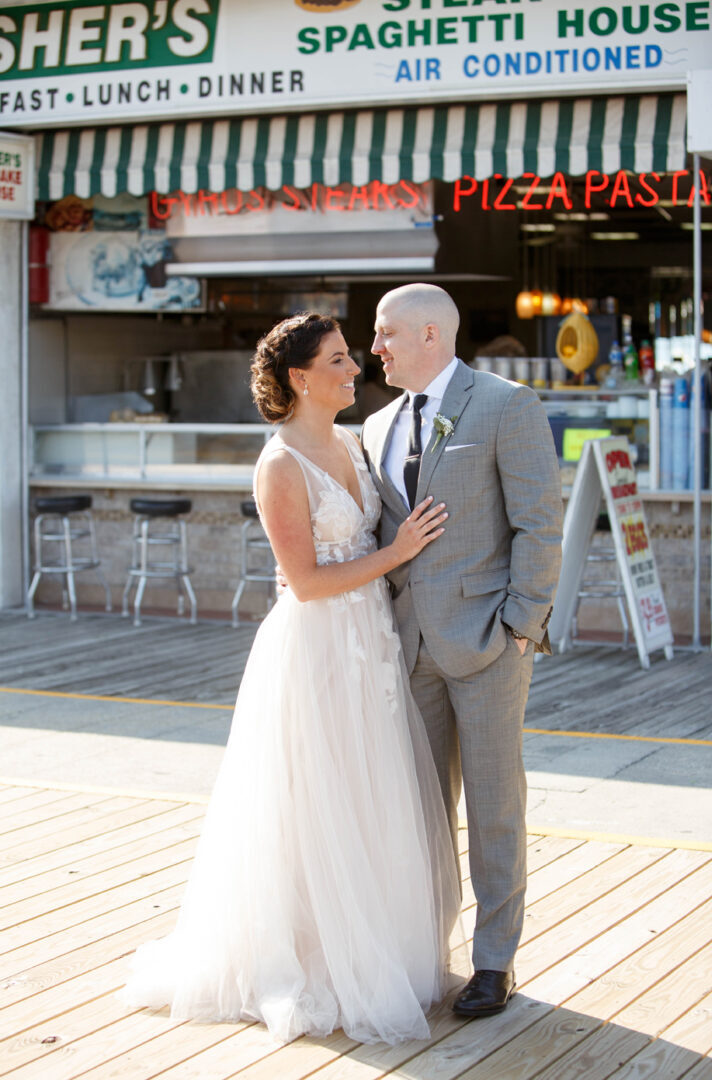 A couple in wedding attire poses in front of a vintage-style pizza and pasta restaurant with a striped awning, capturing the charm of Seaport Pier.