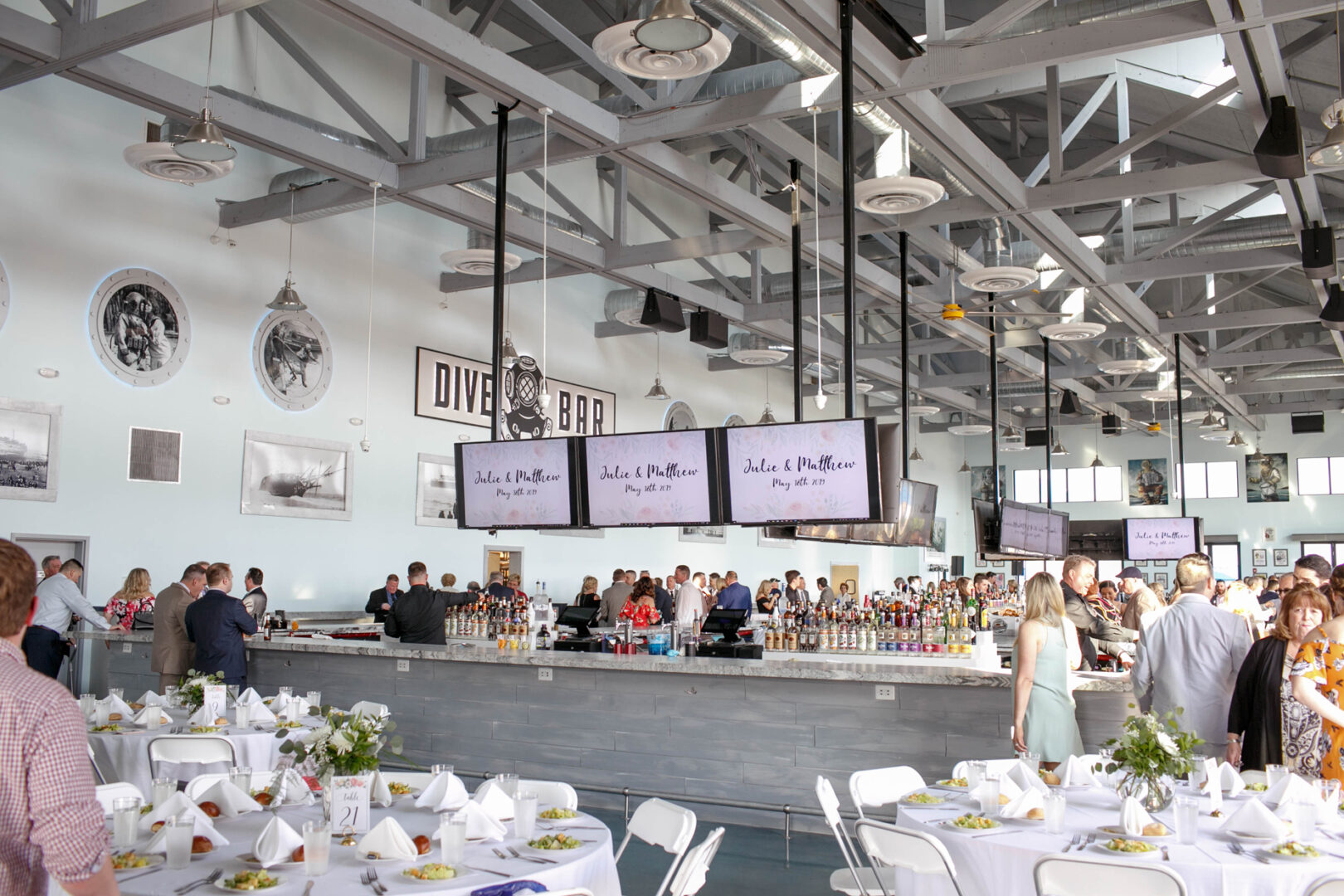 Nestled in the Seaport Pier, this elegant indoor event space features a chic bar and dining tables adorned with white linens, inviting guests to mingle. Multiple screens artfully display information, adding a modern touch to the sophisticated atmosphere.