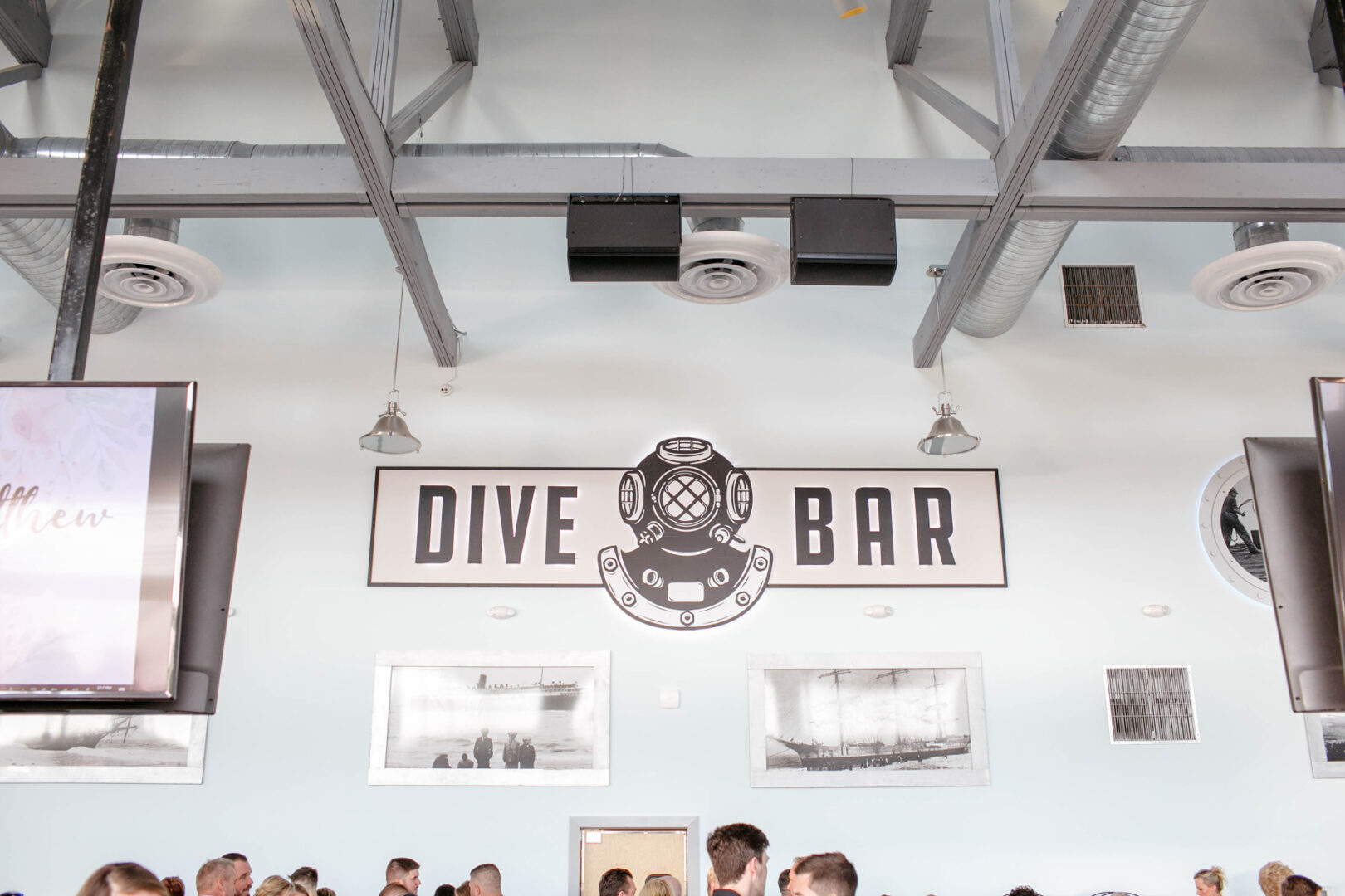 The interior of the bar boasts a "Dive Bar" sign adorned with a vintage diving helmet design, reminiscent of tales from the Seaport Pier, as it casts a nostalgic charm over the lively crowd.