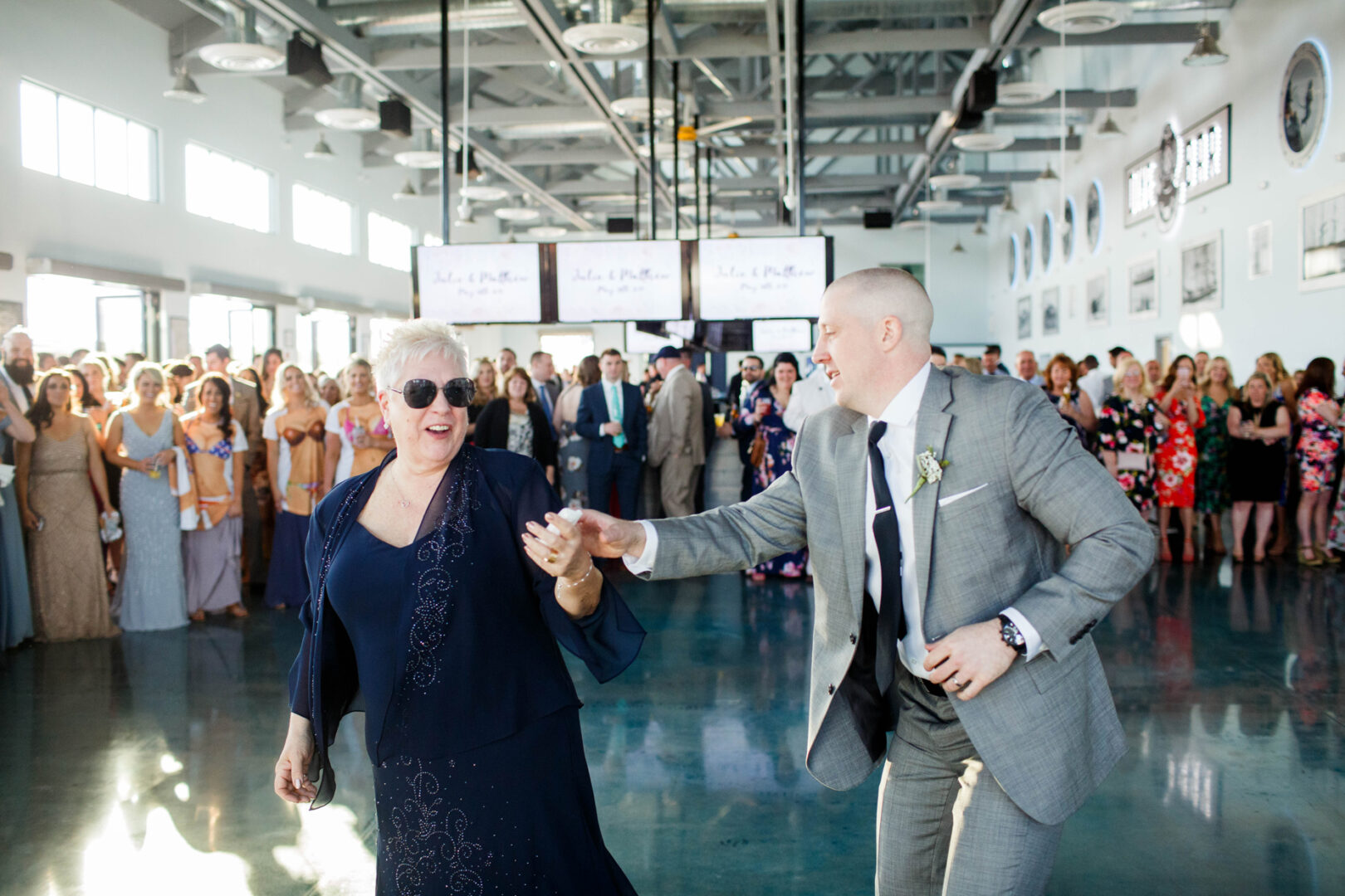 A man and woman dance gracefully in a bright room at Seaport Pier while an captivated crowd watches.