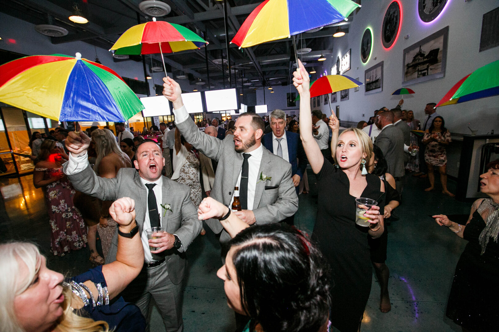 At the lively indoor event, people in formal attire twirled with colorful umbrellas, their movements reminiscent of a vibrant dance at Seaport Pier.