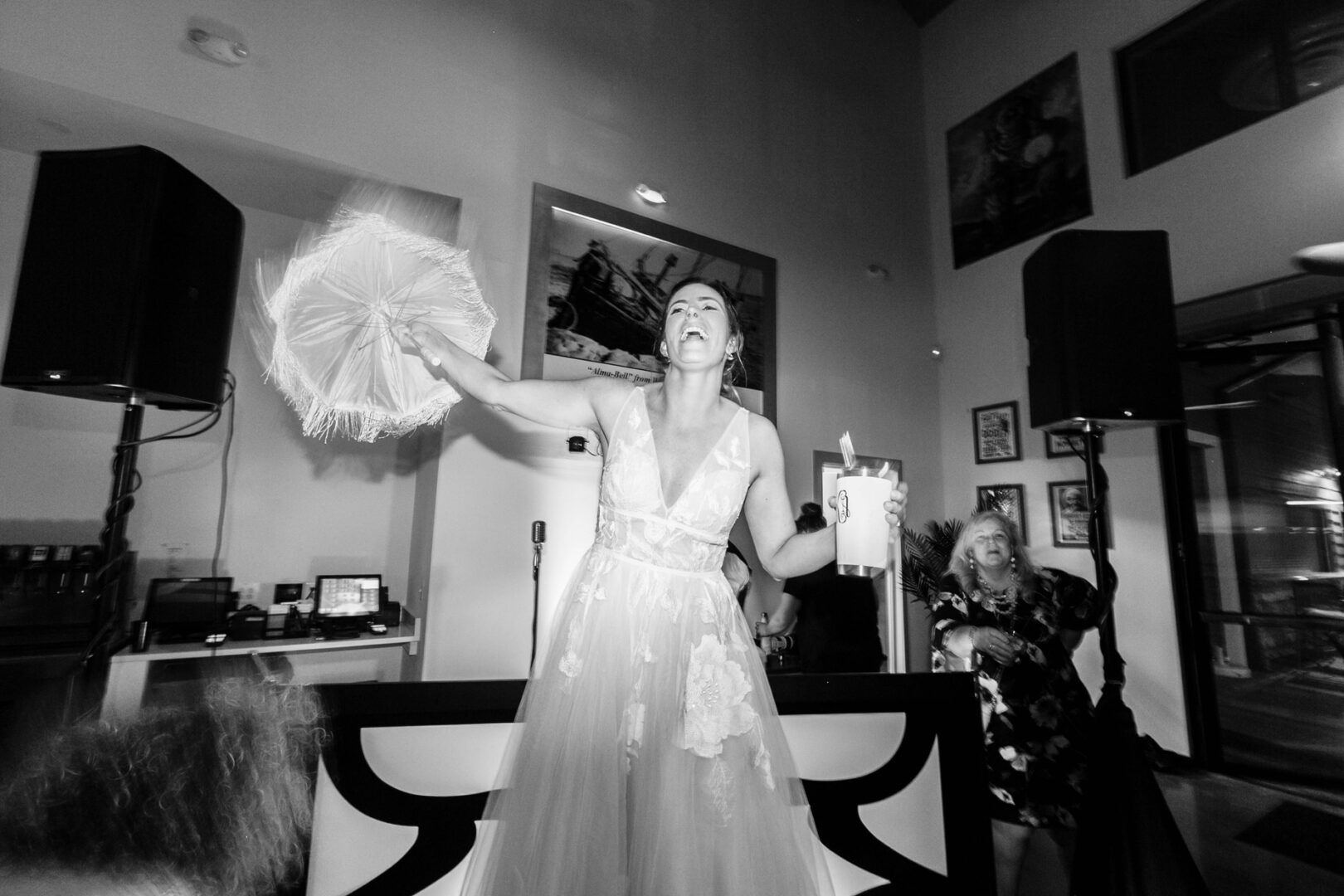 At Seaport Pier, the bride dances energetically, a fan in one hand and a drink in the other, with delighted guests celebrating in the background.