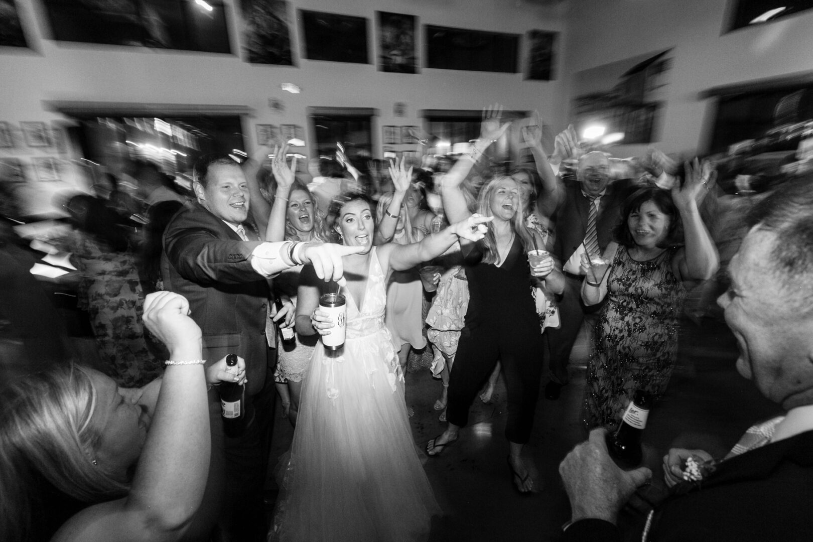 Amidst the vibrant atmosphere of Seaport Pier, a group of people, dressed formally, celebrate and dance with raised hands and drinks in a lively indoor setting.