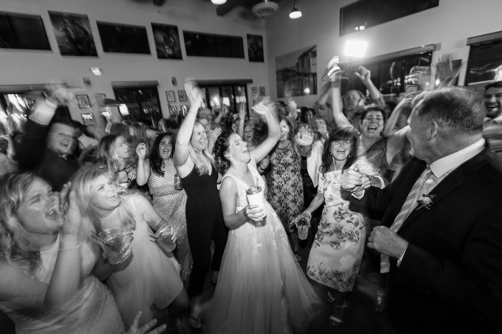 A lively group, including a bride in a wedding dress, is energetically dancing and celebrating indoors at Seaport Pier.