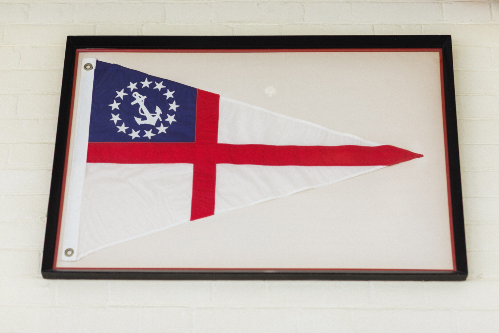 Framed nautical pennant with a red cross, blue field with stars, and anchor design displayed on a white brick wall, perfect for adding charm to your Corinthian Yacht Club of Philadelphia wedding backdrop.