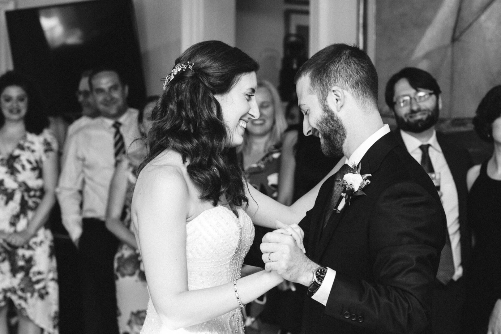Bride and groom smiling and dancing at their wedding reception at the Corinthian Yacht Club of Philadelphia, surrounded by guests watching and clapping. Black and white photo.
