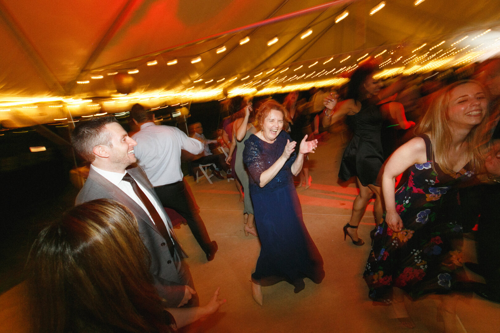 People dancing under string lights at a Corinthian Yacht Club of Philadelphia wedding, with blurred motion capturing the lively and festive atmosphere.