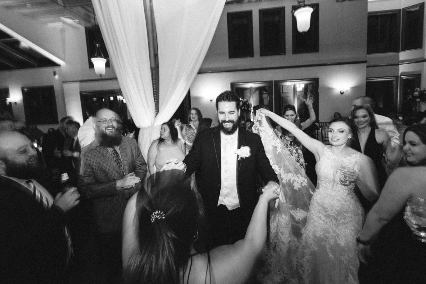 A Knowlton Mansion wedding unfolds in a formal reception hall, where the bride and groom elegantly dance among guests. Laughter fills the air as drinks are raised in celebration, and smiles abound, crafting an enchanting atmosphere that will be cherished forever.
