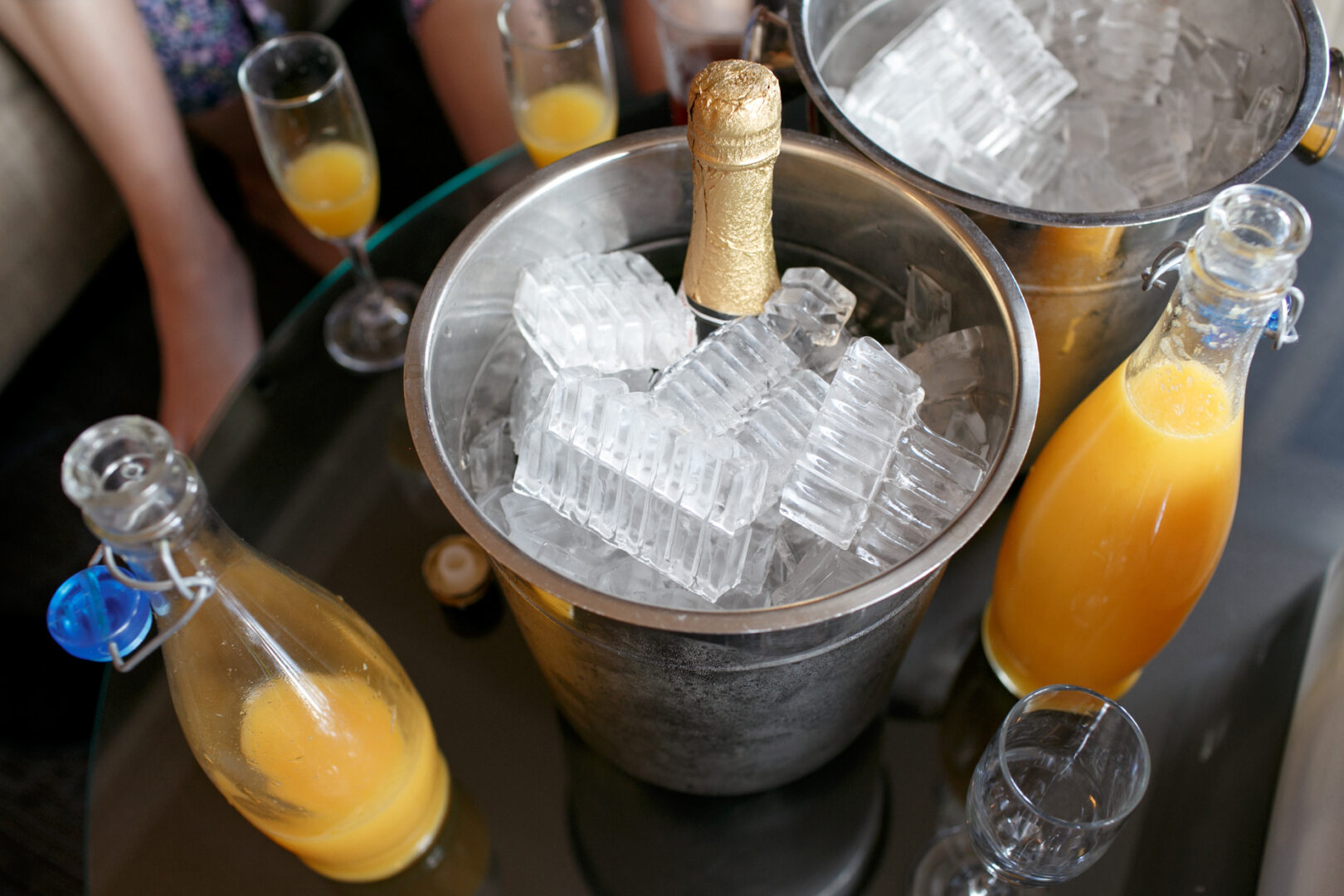 A table set for a Colonial Dames wedding, graced with a champagne bottle in an ice bucket and surrounded by two bottles of orange juice, waits patiently. Four empty champagne flutes stand ready to toast the joyous occasion.
