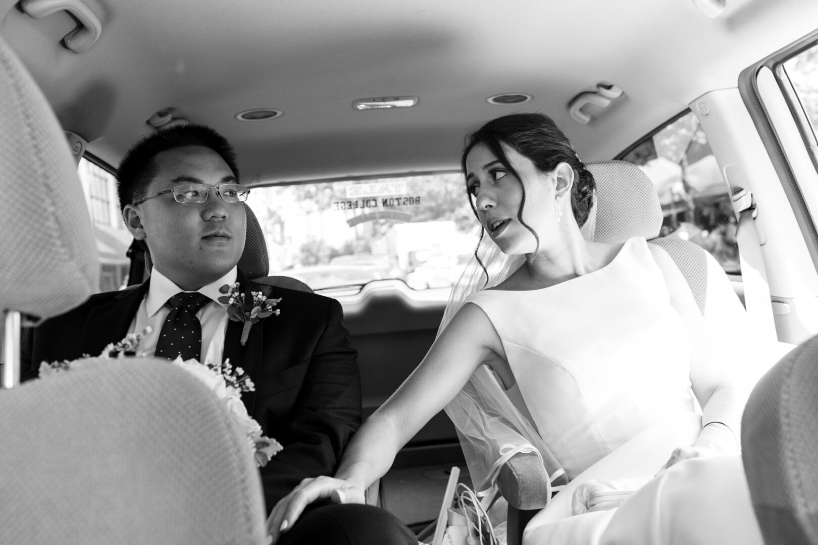 In the backseat of a car, adorned in elegance reminiscent of a Colonial Dames Wedding, the bride and groom share a tender moment, eyes locked and hands gently clasped.