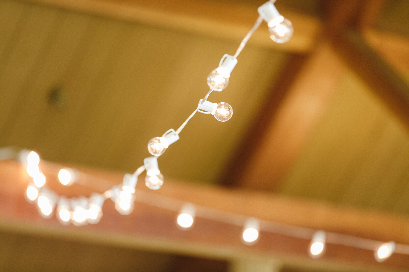 String of white lights hanging from a wooden ceiling, softly glowing in a warm High Point Wedding setting.