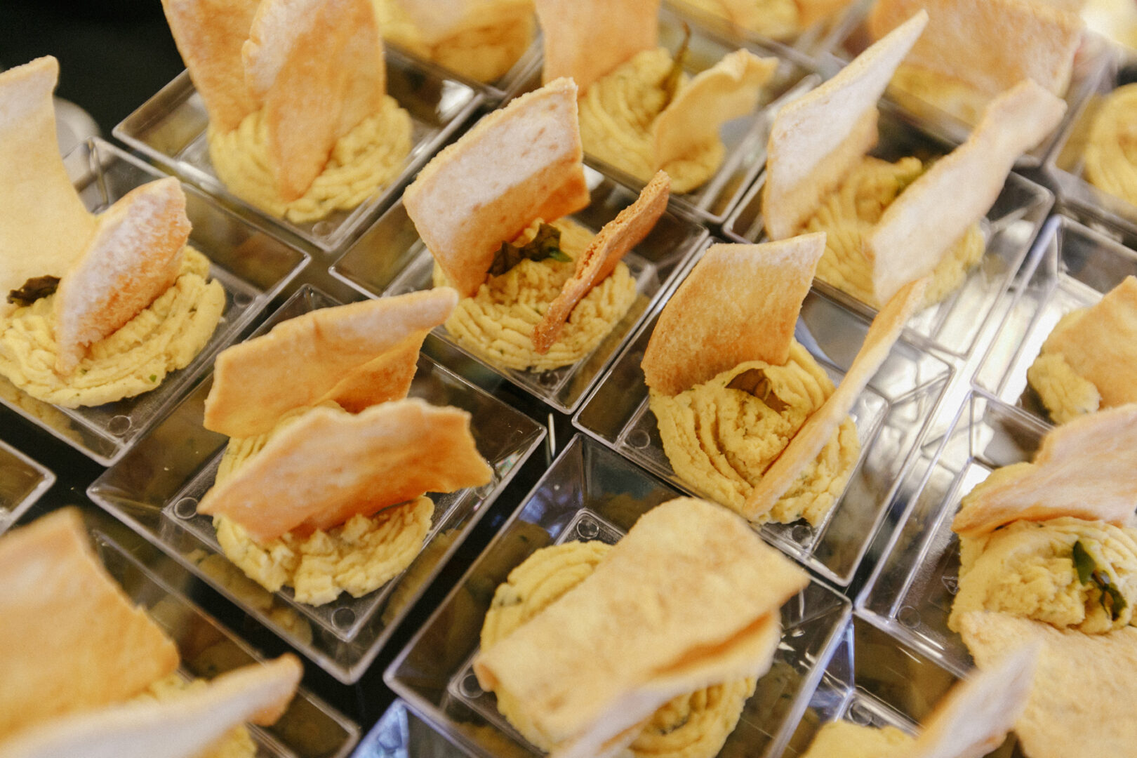 Individual servings of hummus topped with triangular pita chips are elegantly arranged in clear square containers, perfect for a High Point Wedding celebration.