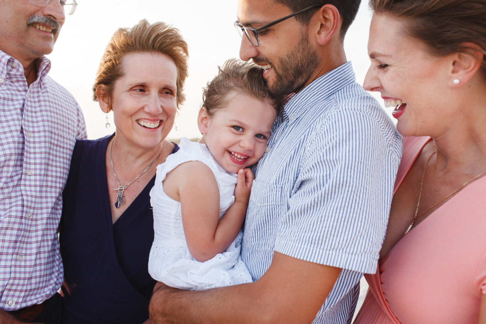 A group of adults and a child are smiling and standing closely together outdoors, capturing the warmth of Cape May family photos.