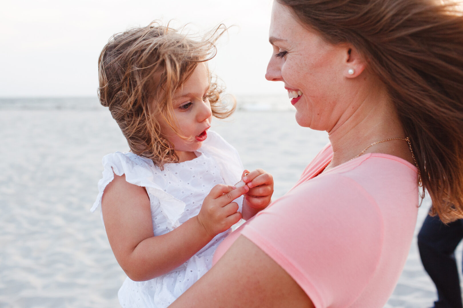 A woman holding a child on the windy Cape May beach, both looking at each other and smiling, captures the essence of cherished family photos.