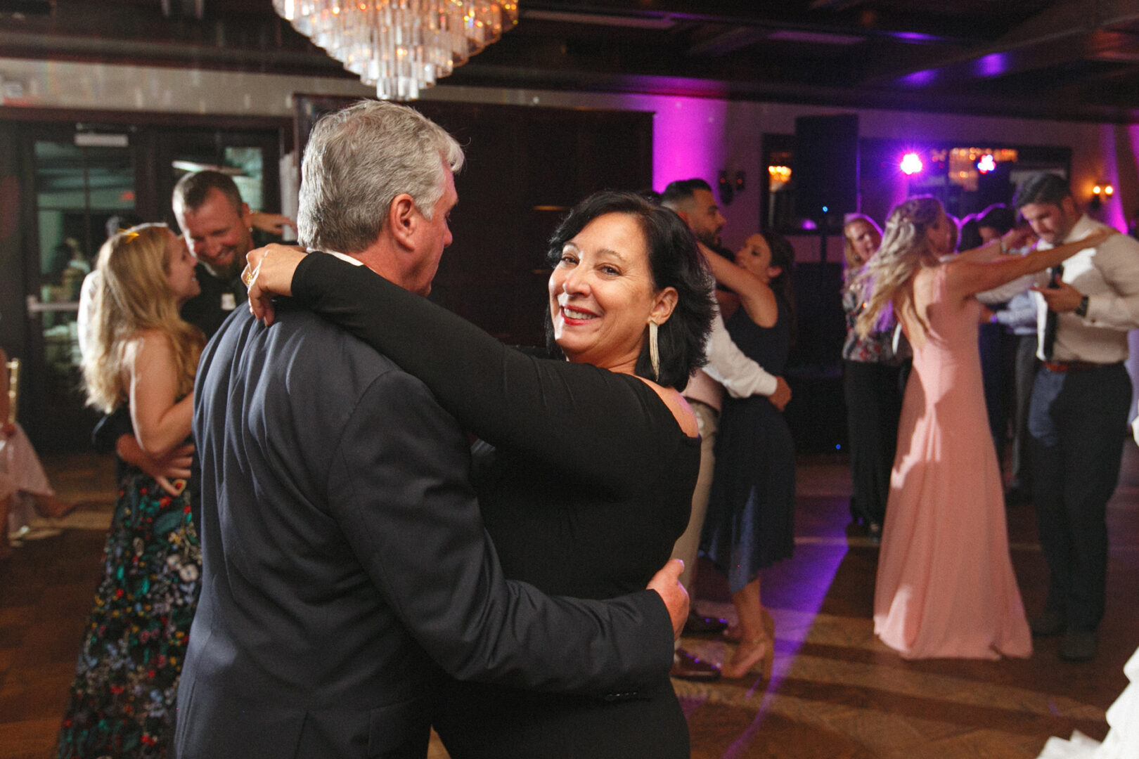 At the elegant Hotel Du Village wedding, couples gracefully twirl in pairs on the dance floor, their sophisticated movements reflecting the event's formality. A woman stands out from the joyful crowd, smiling warmly at the camera, perfectly capturing this beautiful moment.