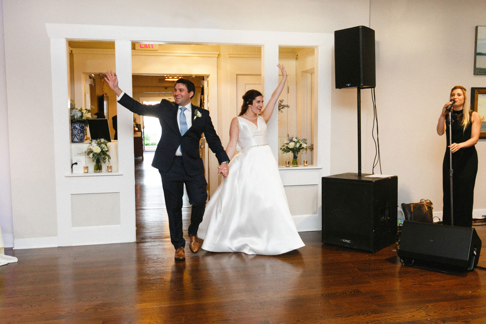 At a Stone Harbor Yacht Club Wedding, a bride and groom enter the room holding hands and waving, while a singer performs to the right.
