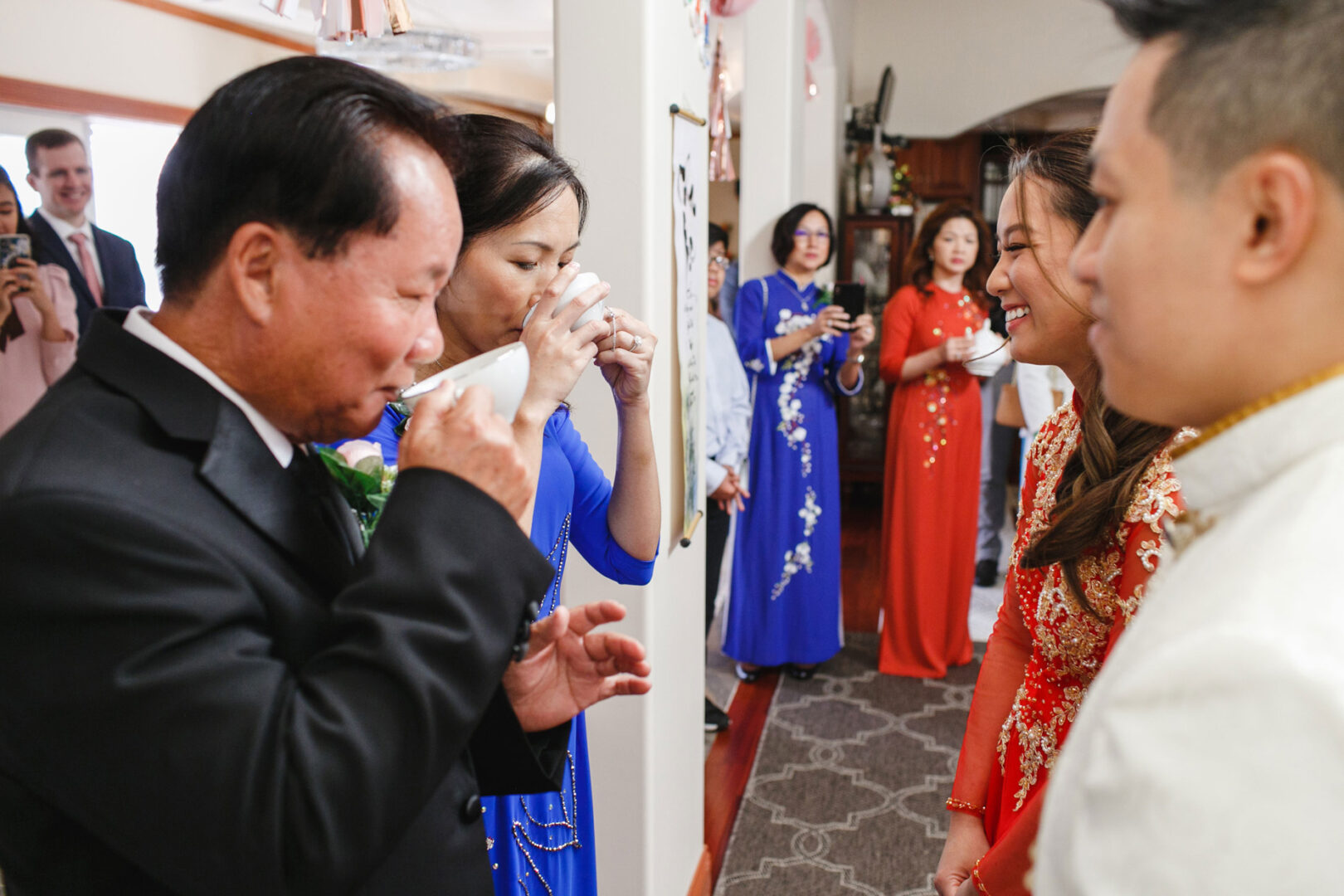 A group of people in traditional attire is elegantly gathered indoors, participating in a serene tea-drinking ceremony reminiscent of a Hershey wedding.