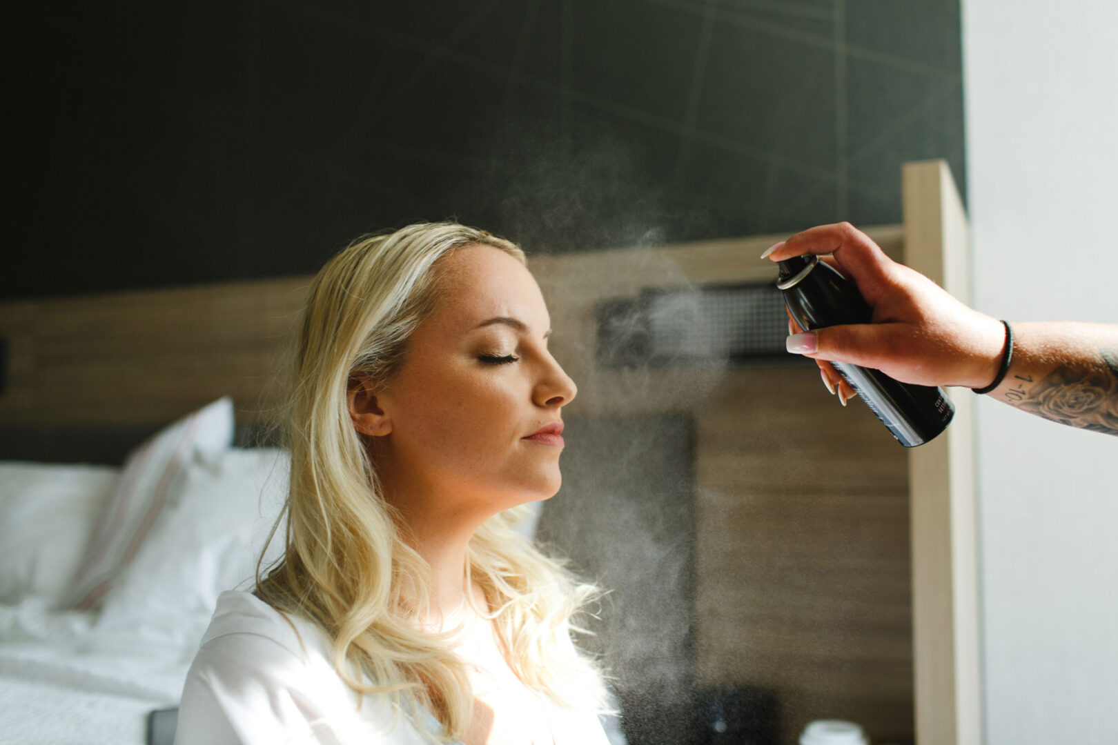In a room with natural light, a person with closed eyes sits serenely as another hand sprays mist over their face, reminiscent of the tranquil moments before a French Creek Golf Club wedding.