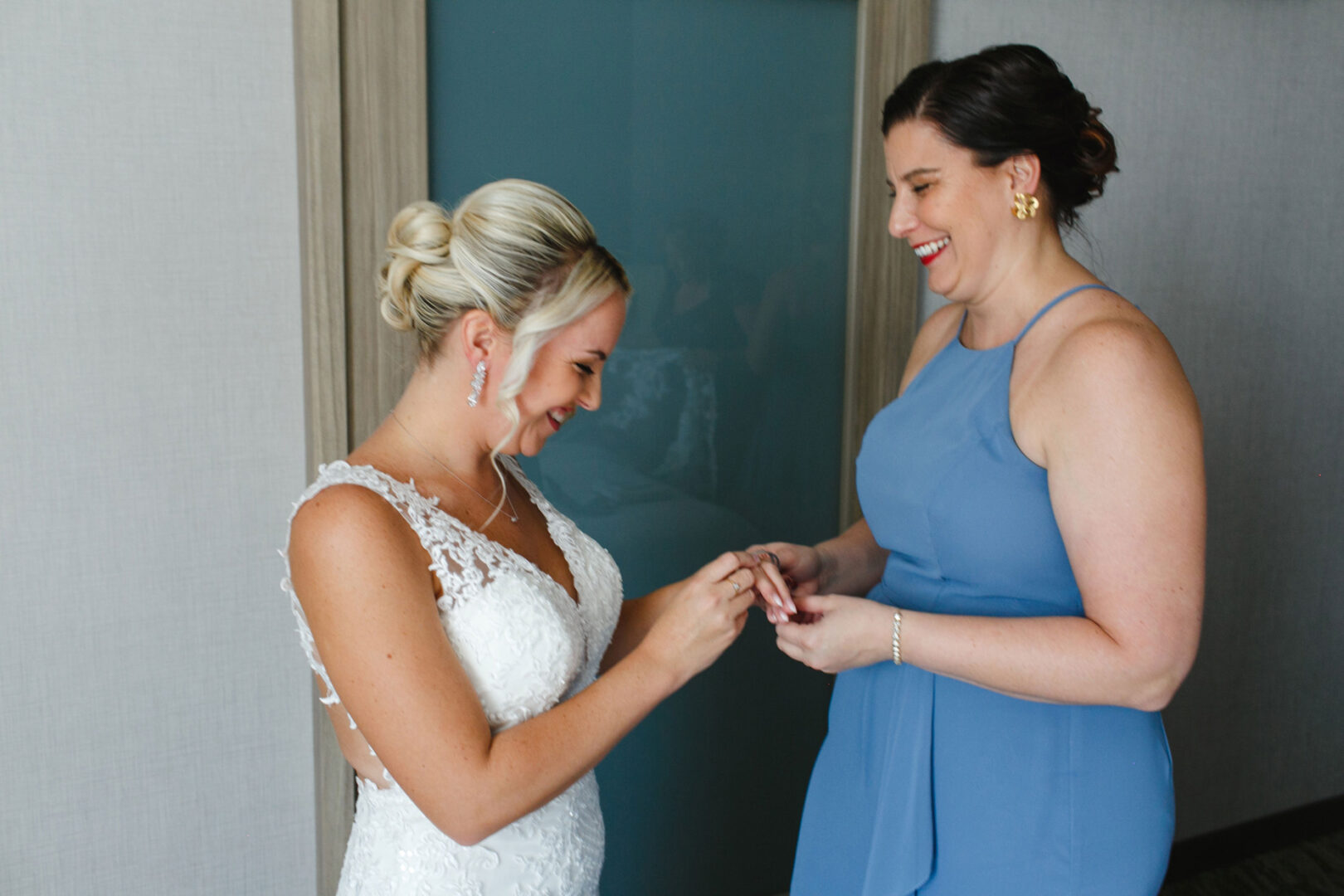 Two women smiling, one in a wedding dress and the other in a blue dress, are exchanging an item at a French Creek Golf Club Wedding.