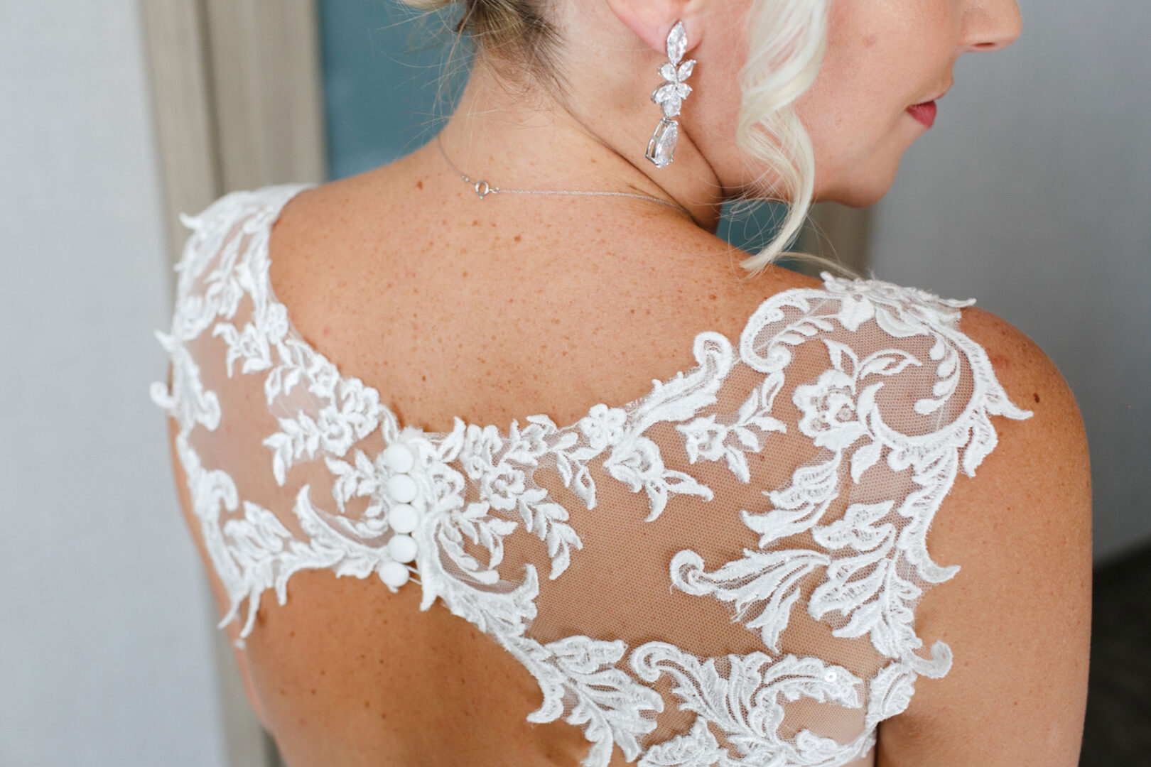 Close-up of a woman in a bridal gown with intricate lace detailing on the back at a French Creek Golf Club wedding. She wears elegant crystal earrings and an updo hairstyle.