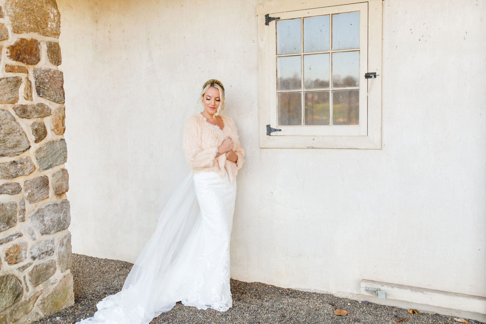 At the picturesque French Creek Golf Club wedding, the bride, adorned in a white dress and light pink shawl, stands elegantly against a stone wall.
