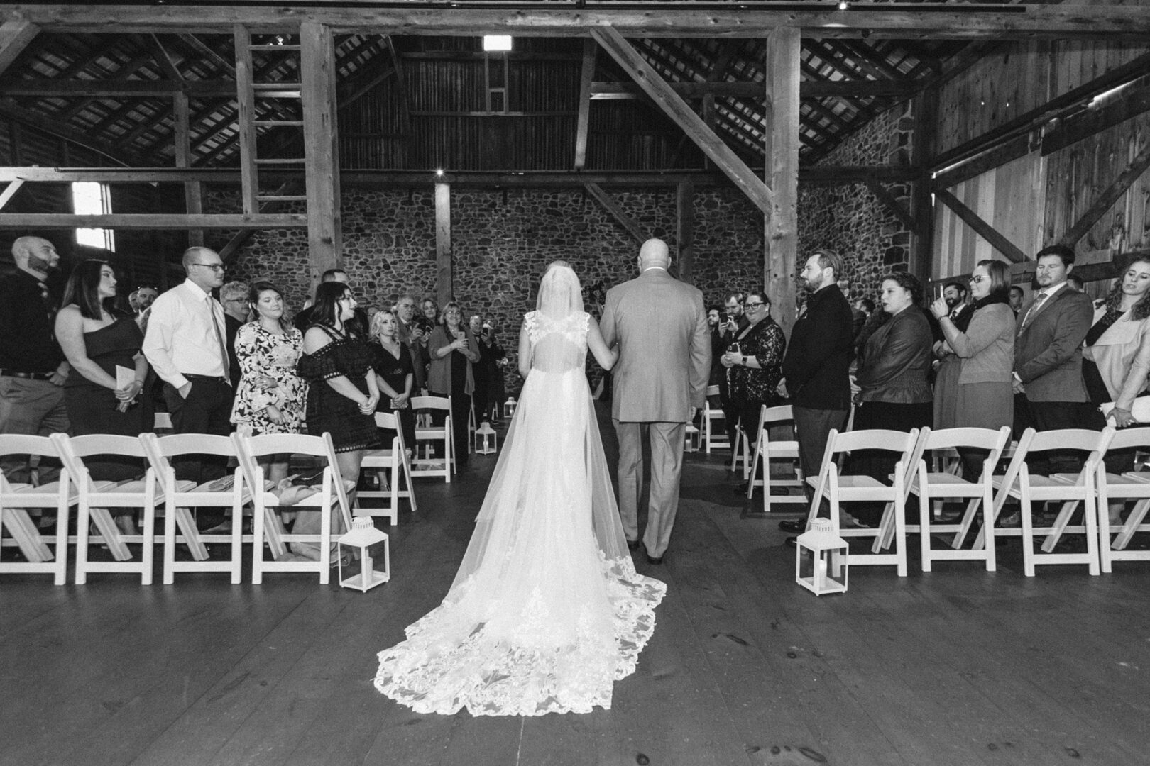 A bride and groom walk down the aisle at a rustic indoor venue, surrounded by friends and family, capturing the essence of a French Creek Golf Club wedding.