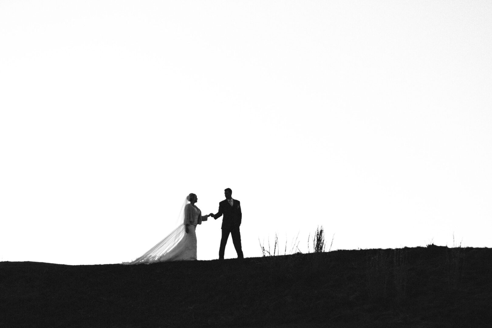 Silhouette of a bride and groom holding hands, standing on a hill against a bright sky at the picturesque French Creek Golf Club Wedding.