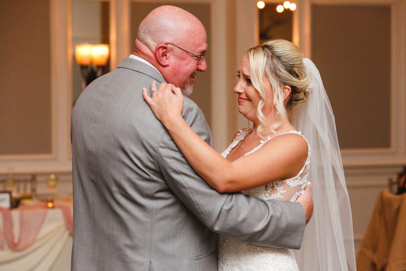 At the French Creek Golf Club wedding, a bride and an older man in a gray suit share a dance, gazing at each other in the warmly lit room.