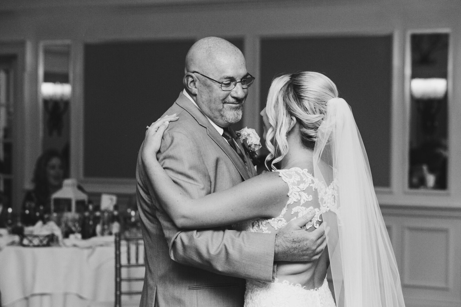 In the elegant ambiance of a French Creek Golf Club wedding, a bride and an older man share a dance. She wears a lace gown with a veil, while he dons a sharp suit, capturing the timeless moment under the venue’s enchanting charm.