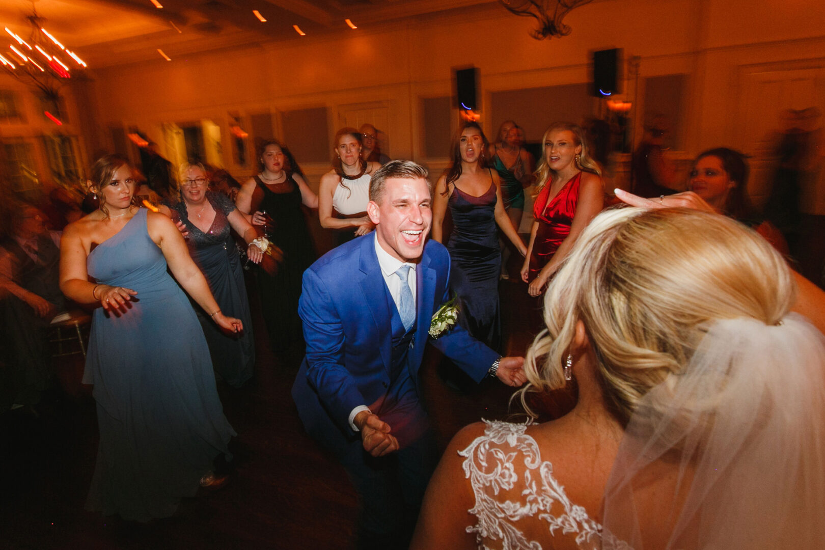At the lively French Creek Golf Club wedding, a groom in a blue suit dances energetically with a group of people, including the bride in the foreground.