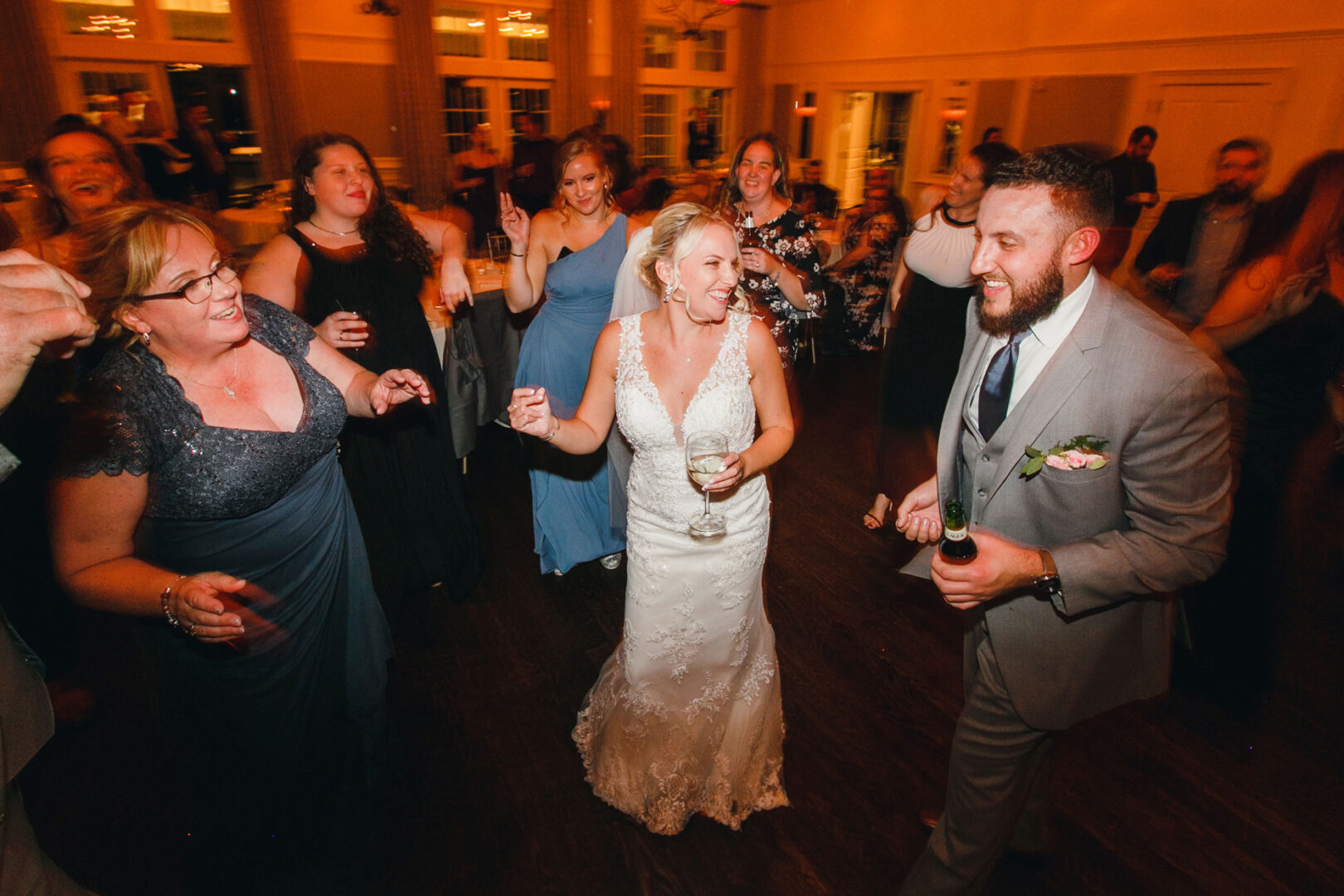 At a French Creek Golf Club wedding, the bride and groom dance joyfully, surrounded by guests in a warmly lit room.
