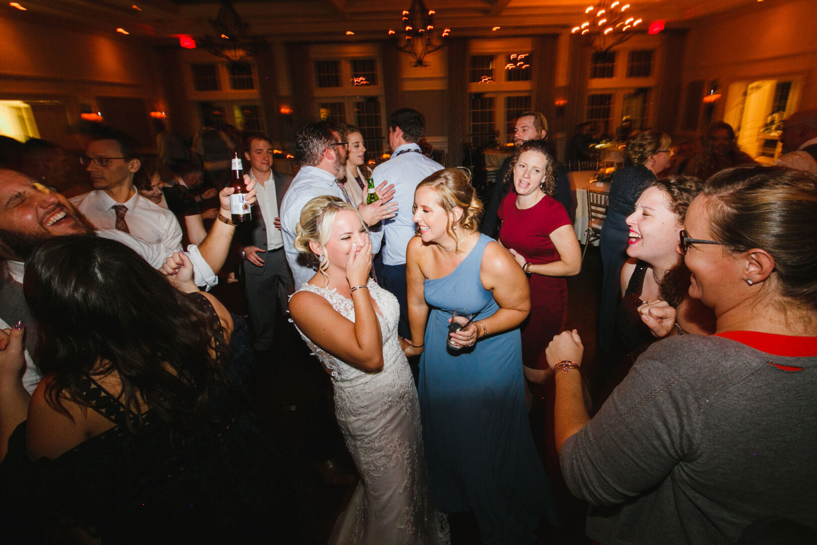 At a lively indoor wedding reception at French Creek Golf Club, the bride and guests are joyfully dancing and laughing together.
