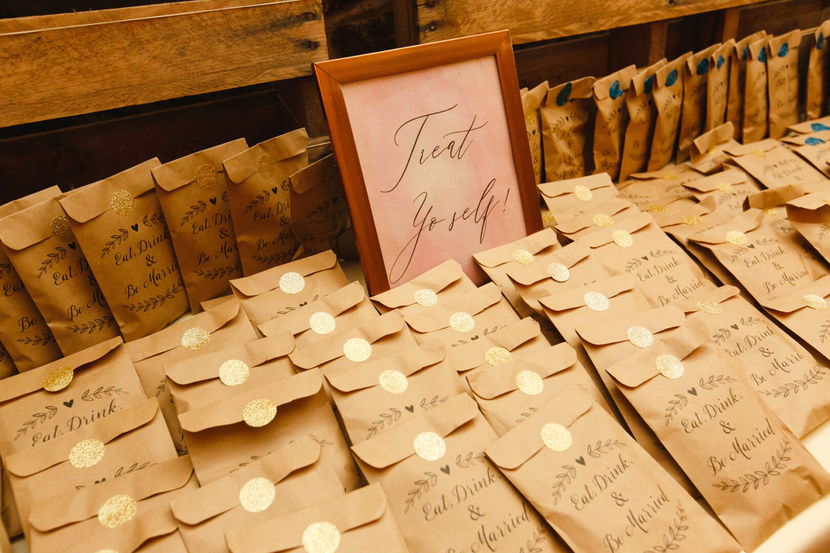 A table displays numerous brown paper bags with golden seals beside a framed sign that reads "Treat Yo'self!"—a delightful touch at the French Creek Golf Club Wedding.