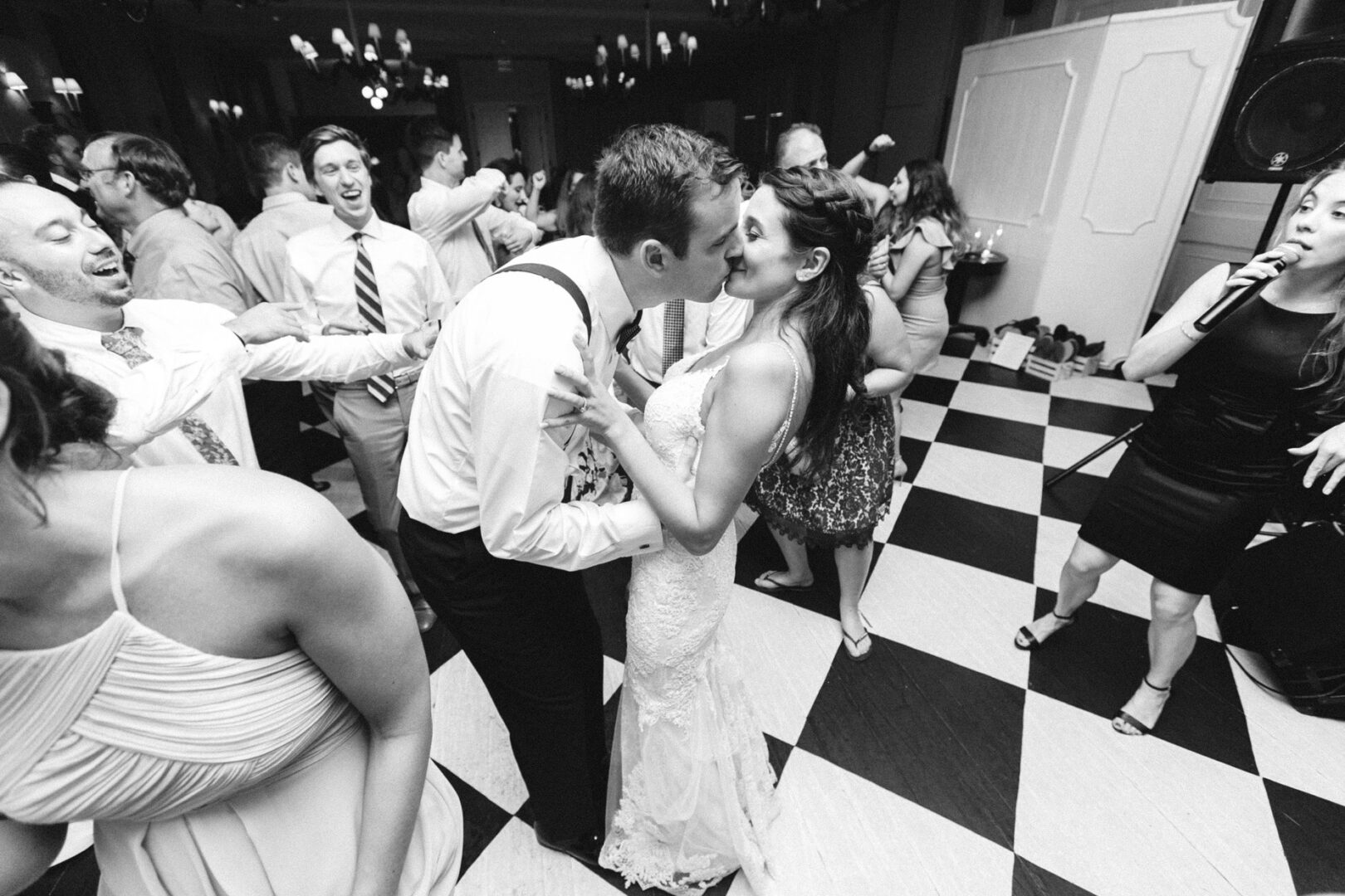 A couple kisses on a checkered dance floor surrounded by a lively crowd at their Cape May wedding reception.