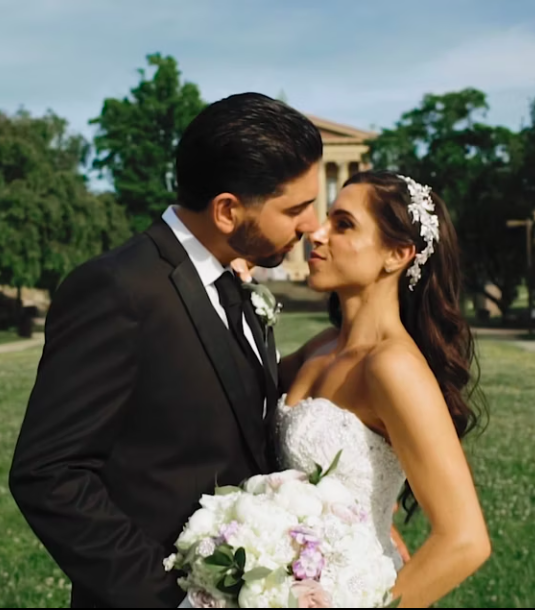 Under a sunlit sky, the bride and groom share a tender kiss, captured perfectly for their Vie Wedding Video. She clutches a delicate bouquet, both of them resplendent in formal wedding attire.
