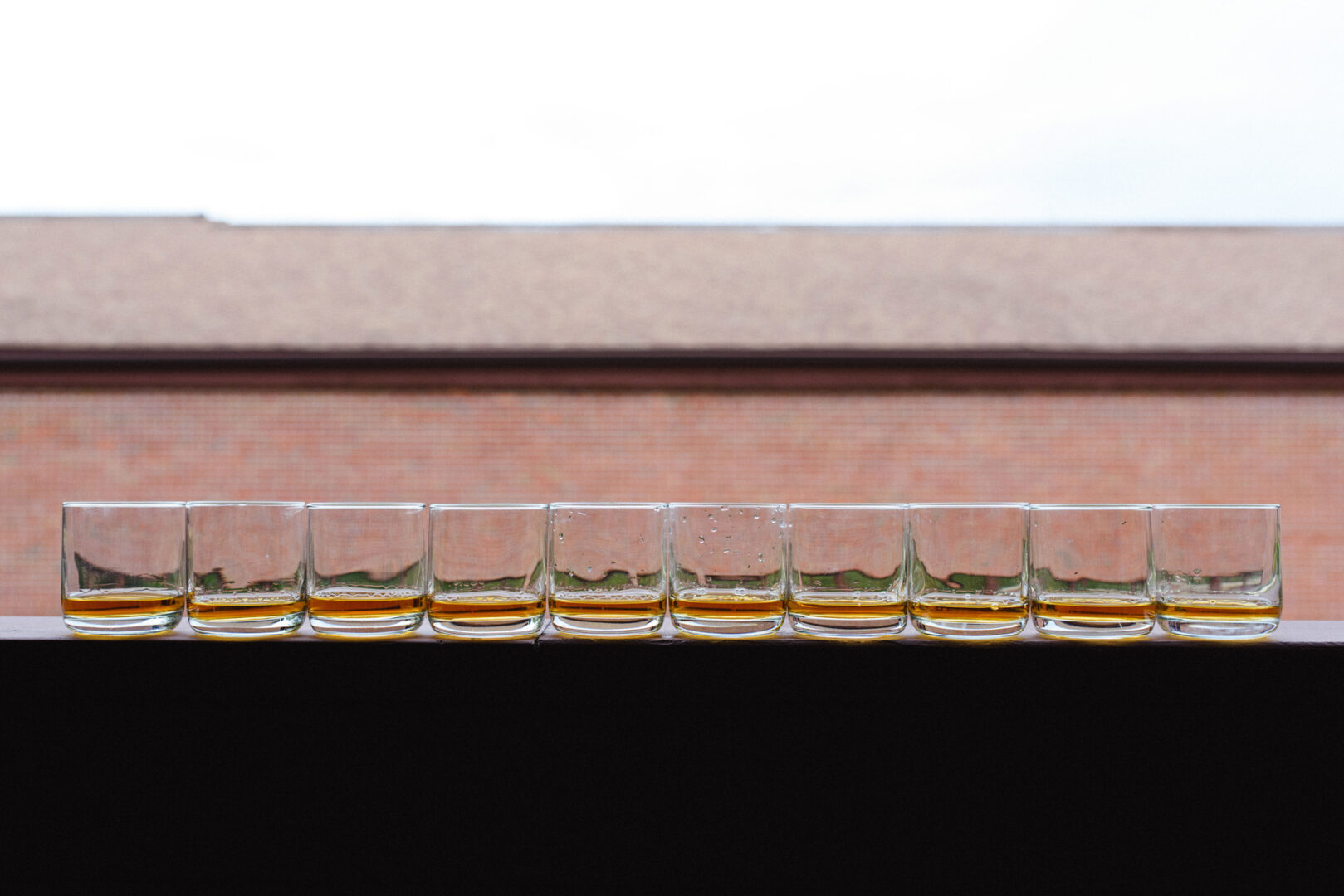 On a ledge at the Union League at Liberty Hill Wedding, a row of twelve whiskey glasses gleam, with a blurred building in the background.
