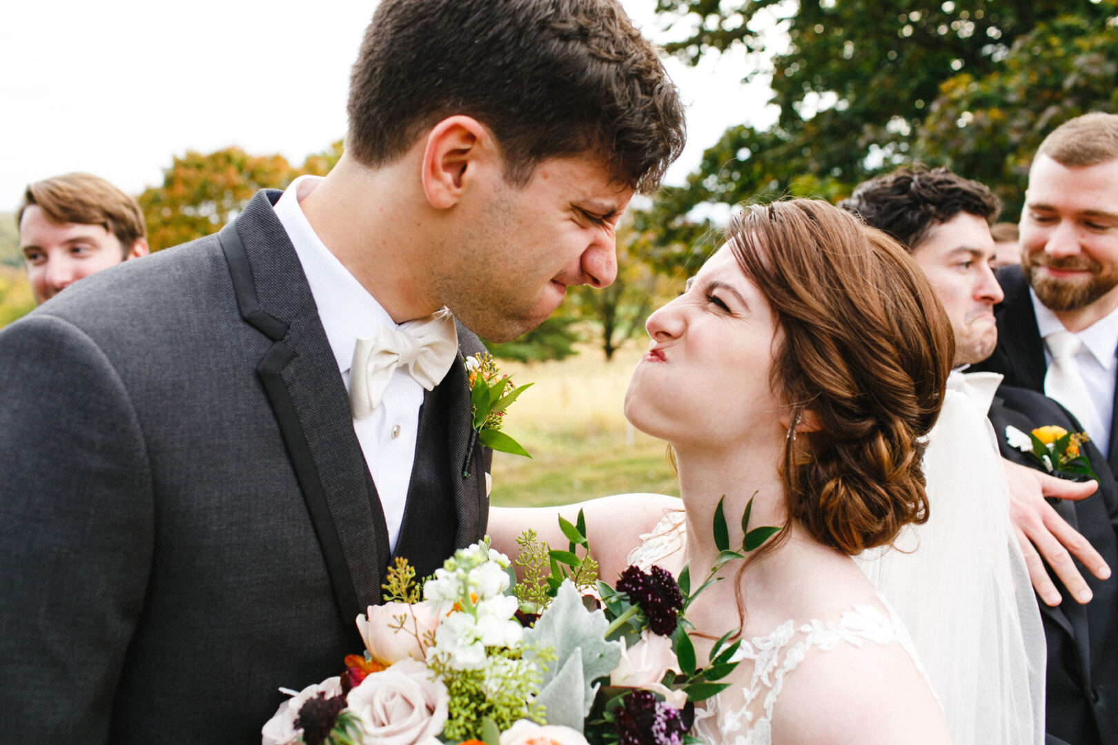 At their Union League at Liberty Hill wedding, the bride and groom exchange funny faces amidst a backdrop of groomsmen. The bride, clutching a bouquet of flowers, radiates joy and playfulness on this special day.
.