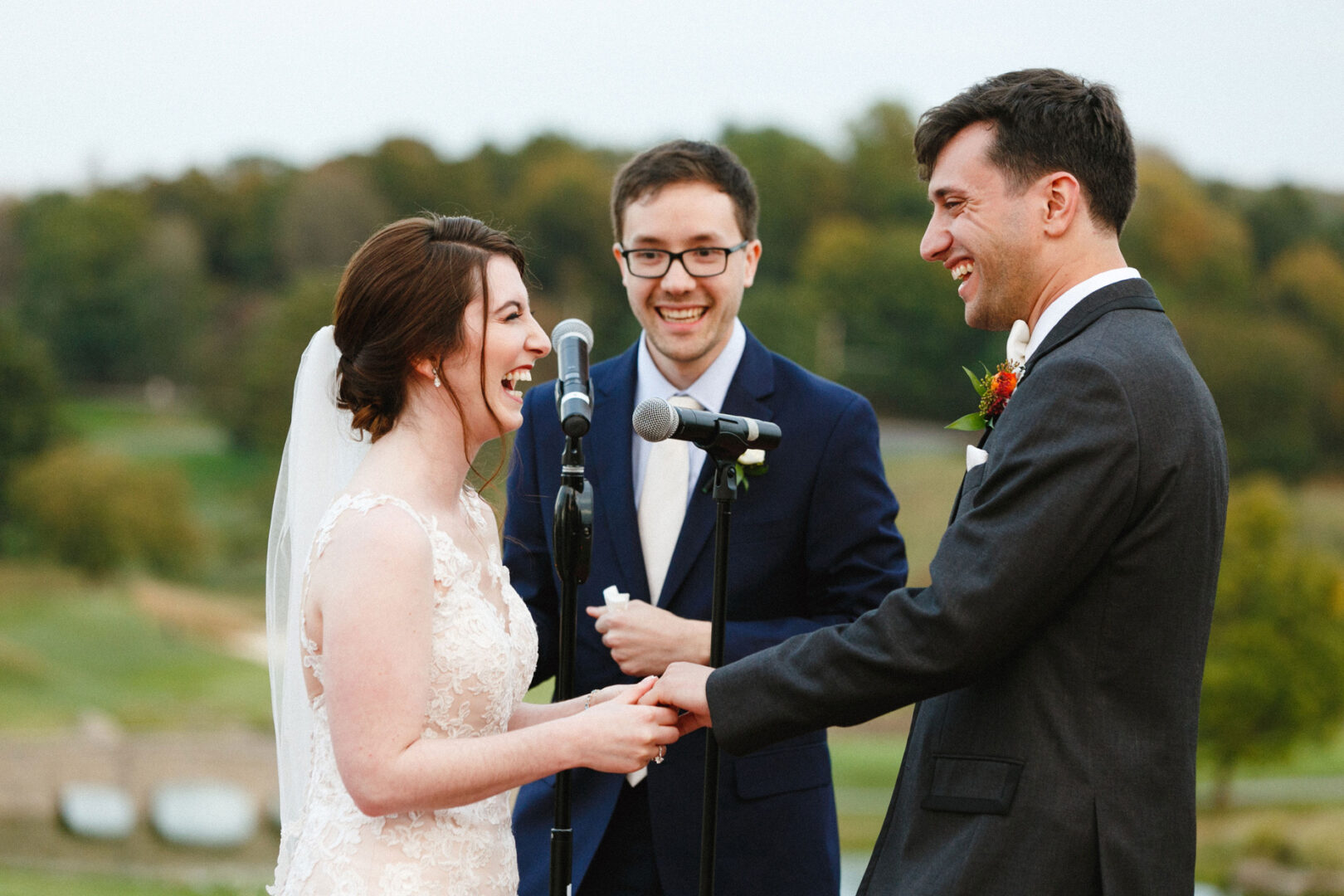 During a Union League at Liberty Hill Wedding, a bride and groom hold hands and smile at each other, with an officiant standing between them under the open sky.
