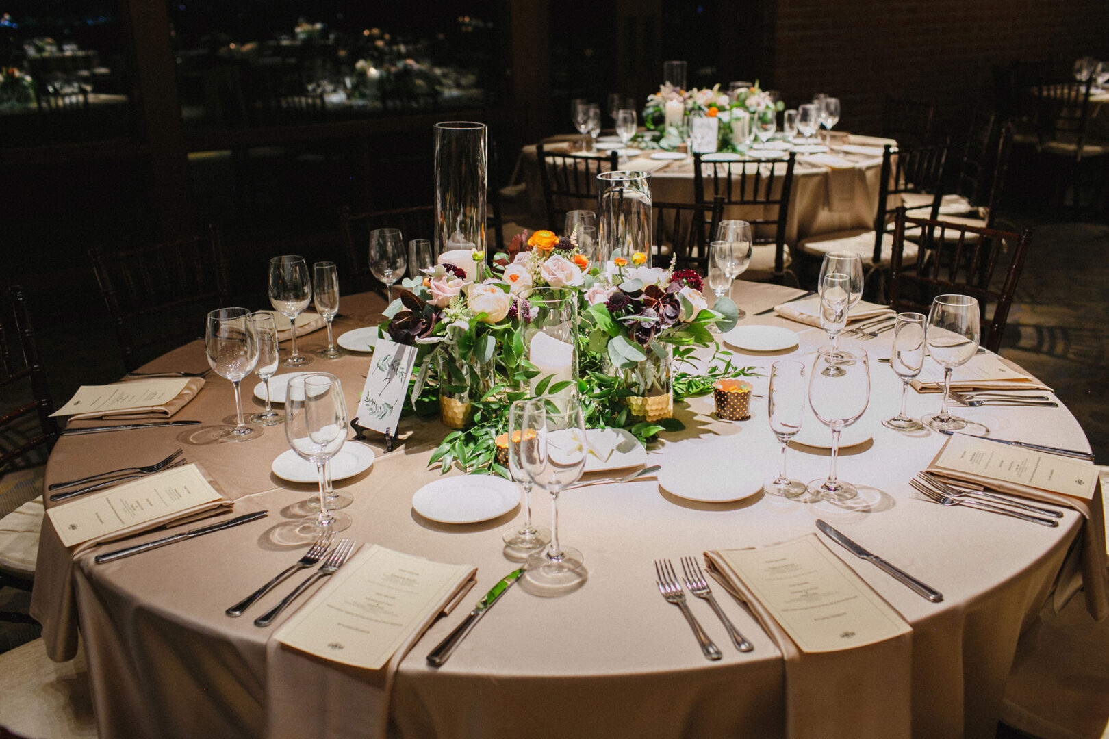 Elegant table setting for a Union League at Liberty Hill wedding, featuring a floral centerpiece, glassware, and menus on a round table with beige tablecloth.