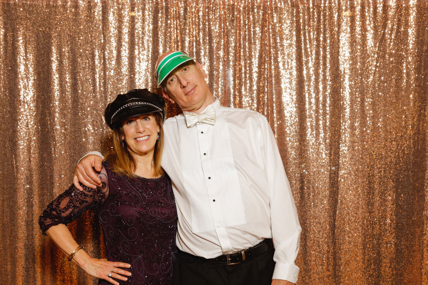 A man and woman wearing hats pose with arms around each other in front of a glittering backdrop, reminiscent of a joyous Union League at Liberty Hill wedding.