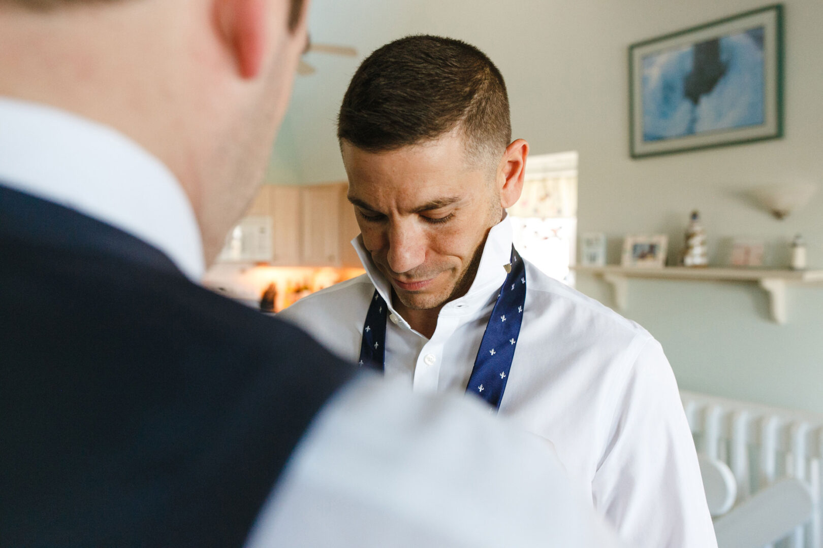 A man in a white shirt is getting his tie adjusted by another person, reminiscent of preparations before a big event at the Yacht Club of Sea Isle City. They are indoors with a softly lit background, capturing the elegance of wedding festivities.