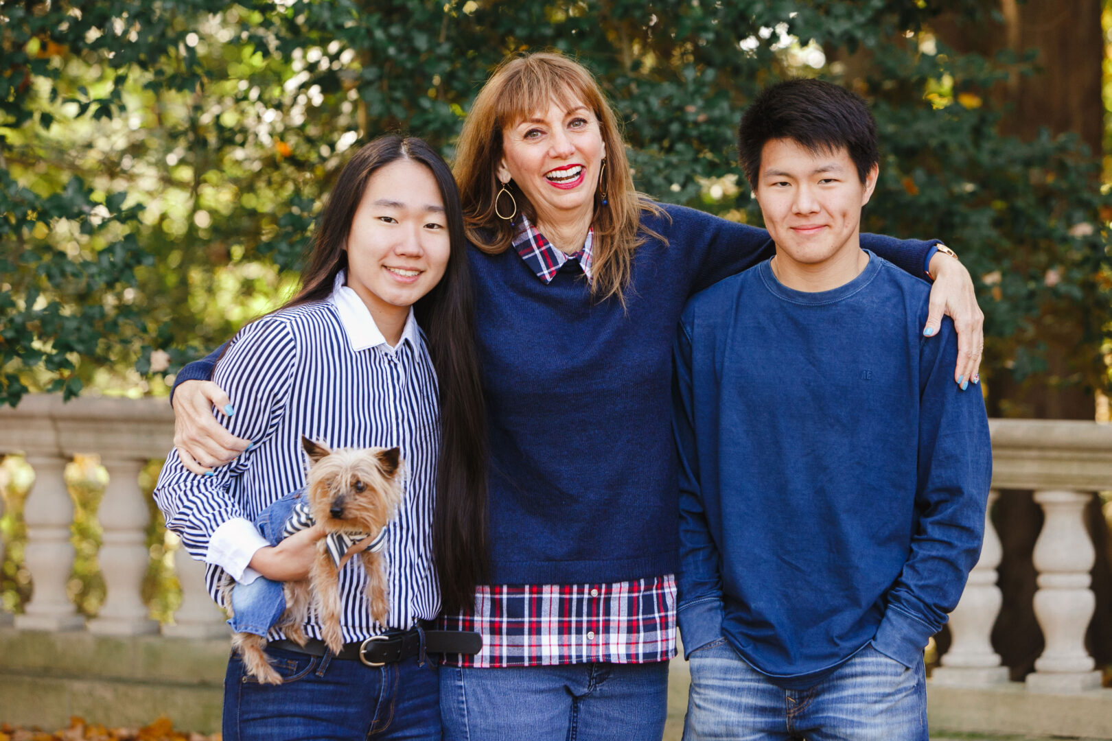 Three people and a small dog pose together in front of a stone railing, surrounded by lush greenery—the perfect setting for capturing the best Philadelphia family photos.