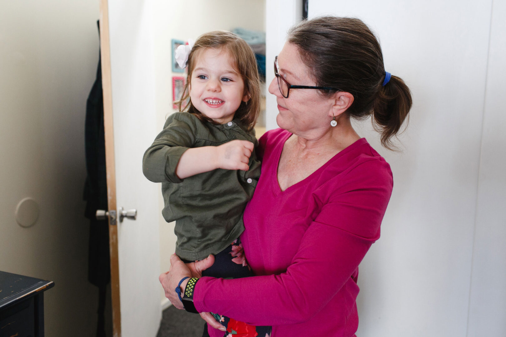 A woman cradles a smiling child indoors, gently standing near an open door, capturing the warmth of a Newborn Session in Philadelphia.