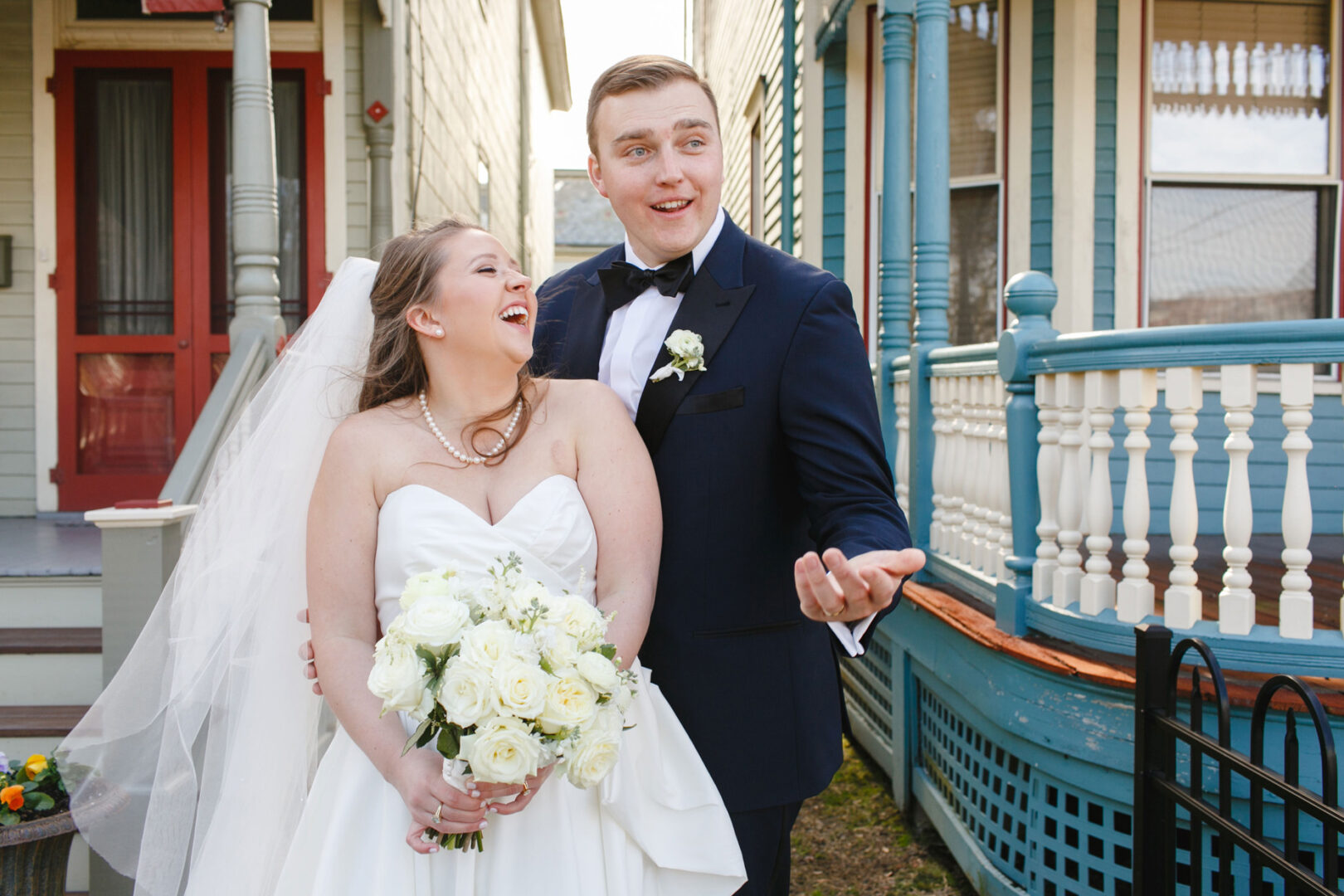 A bride and groom stand smiling outside a grand house, dressed in their beautiful wedding attire, reminiscent of a mesmerizing Congress Hall wedding. The bride holds a bouquet of elegant white flowers.