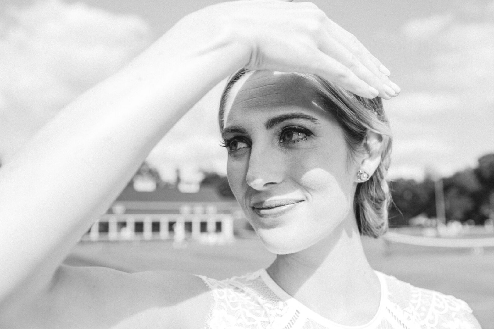 A woman shields her eyes from the sun with her hand as she stands outdoors in front of a building, capturing the elegant charm of a Philadelphia Cricket Club wedding.