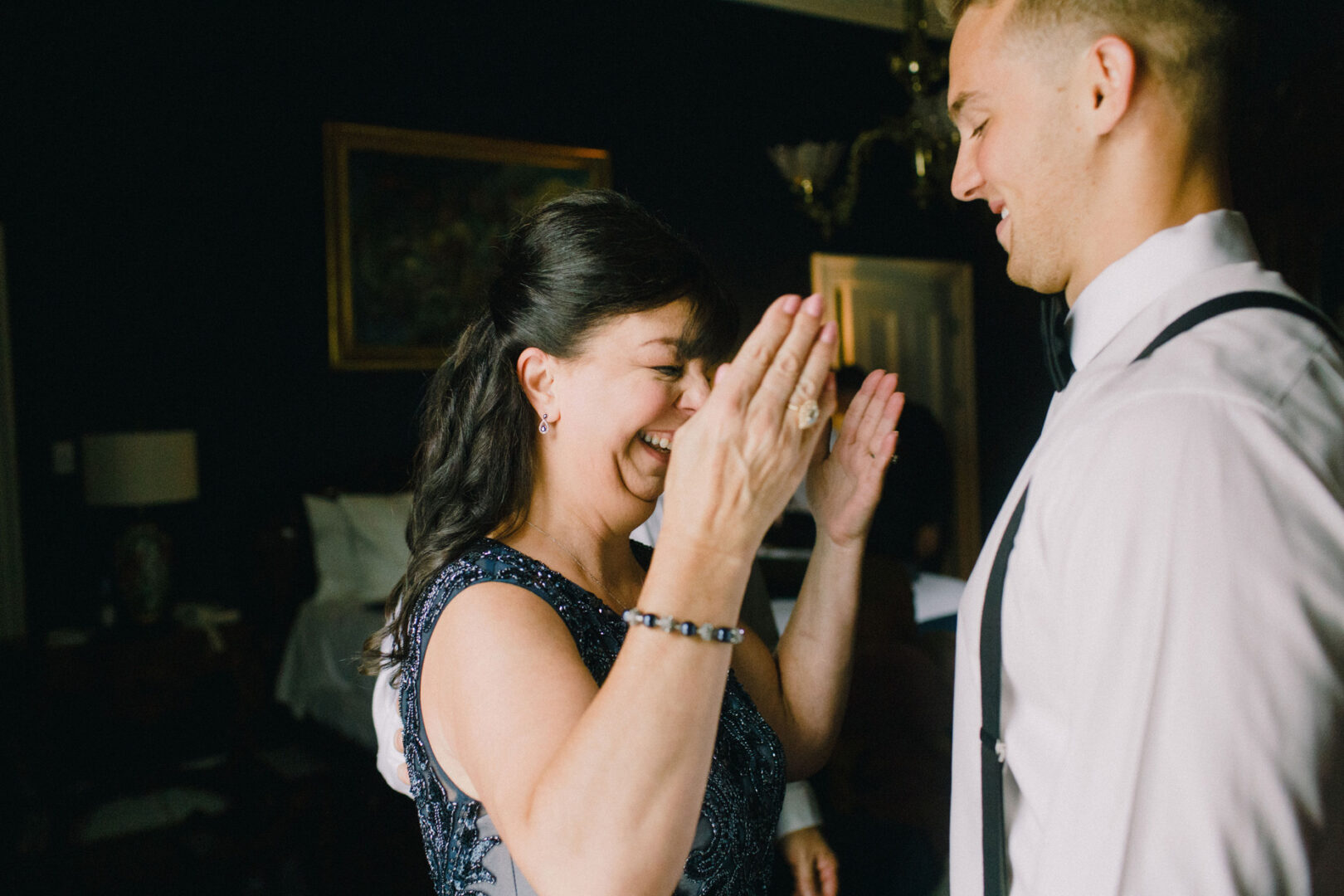A woman claps joyfully at a Willow Creek Winery wedding, facing a smiling man in formal attire in the dimly lit room.